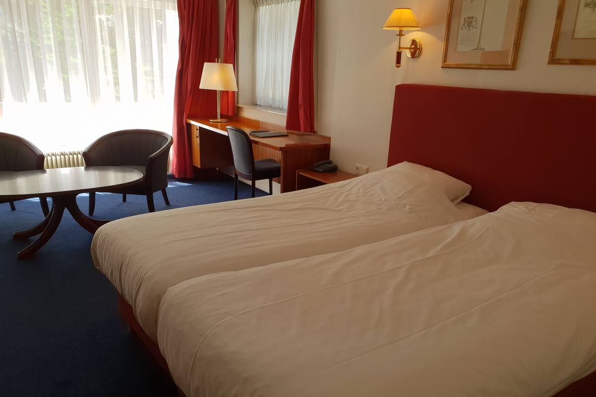 A hotel room with a bed, a desk, a chair, a lamp, and a window with curtains.