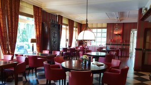 A hotel dining area with checkered flooring, red chairs, and a large round table with a vase of flowers. - Nol in 't Bosch (Wageningen)