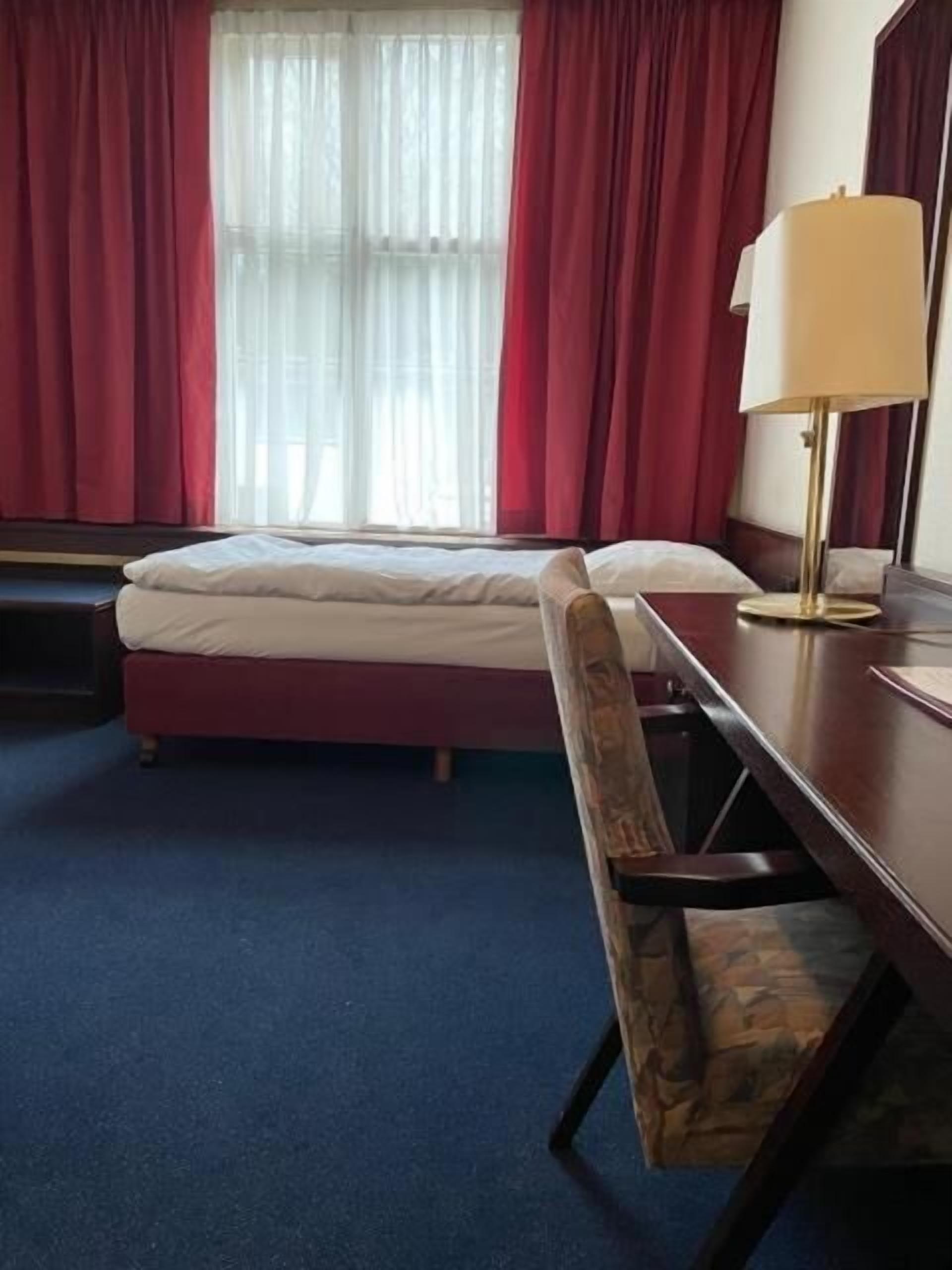 Una habitación de hotel con cama, escritorio, silla y lámpara.
