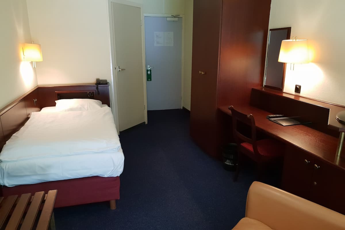 A hotel room with a bed, a desk, a chair, a desk lamp, and a mirror.