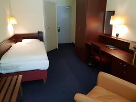 Habitación de hotel con una cama, un escritorio, una silla, una lámpara de escritorio y un espejo.