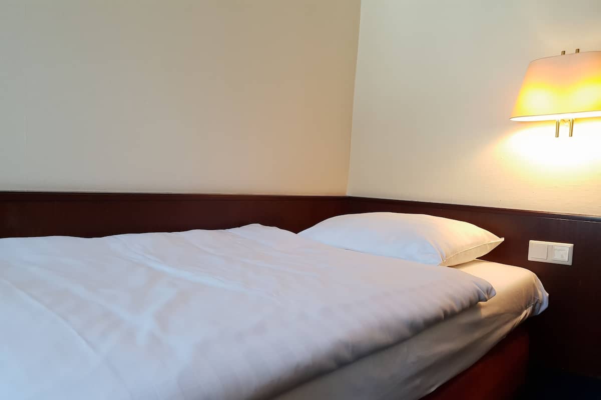 A neatly made bed with white linens and a wooden headboard in a hotel room.