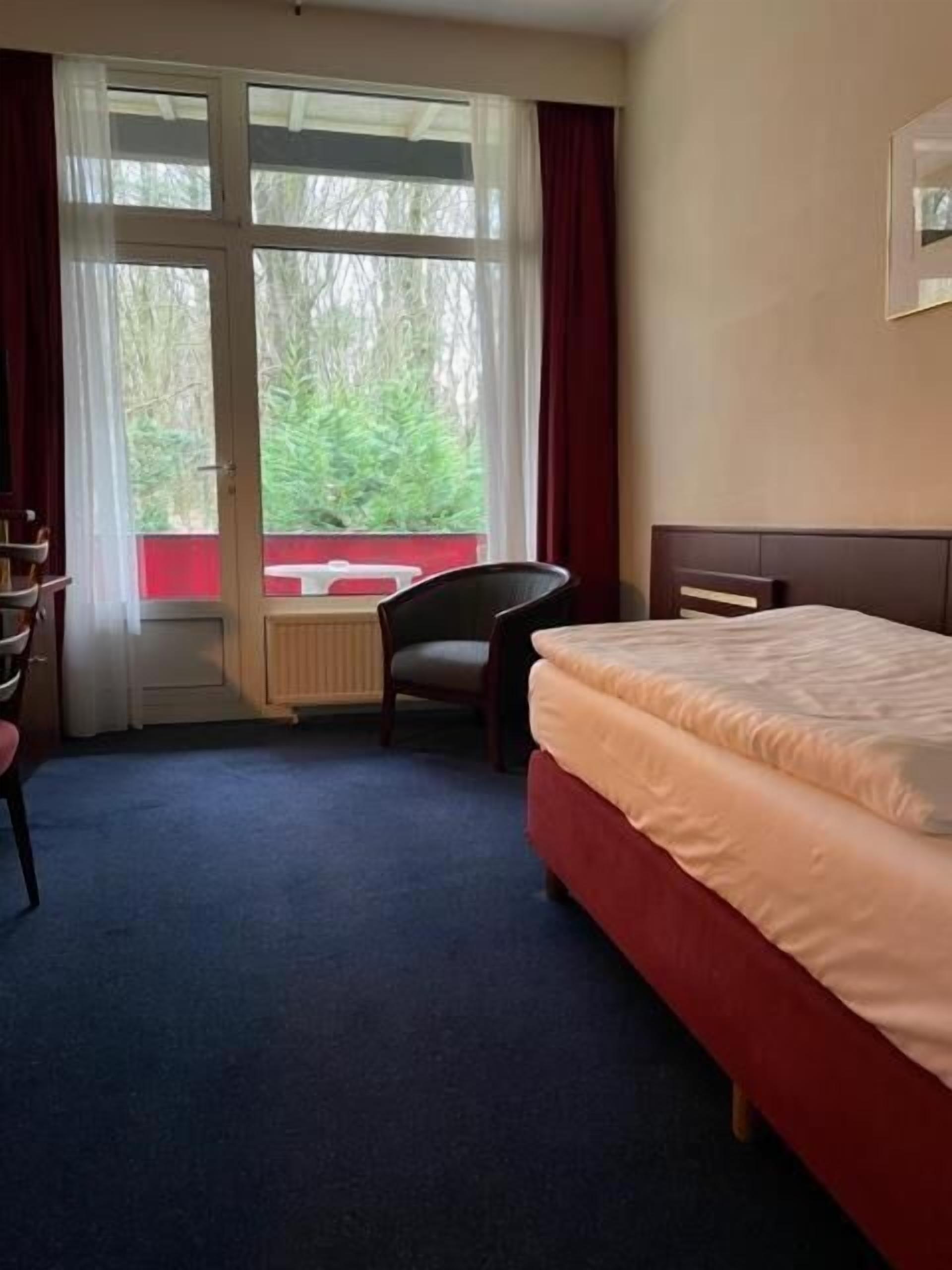 A hotel room with a bed, a chair, a desk, and a window with curtains.