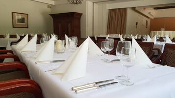 Een eetruimte met gedekte tafels voor een formeel diner, met witte tafellinnen, glazen en bestek.