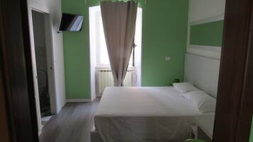 Une chambre à coucher avec un lit, un téléviseur fixé au mur et une fenêtre avec des rideaux.