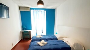 A hotel room with two beds, a desk, a chair, a nightstand, and a window with curtains. - Smart Rooms (Trieste)