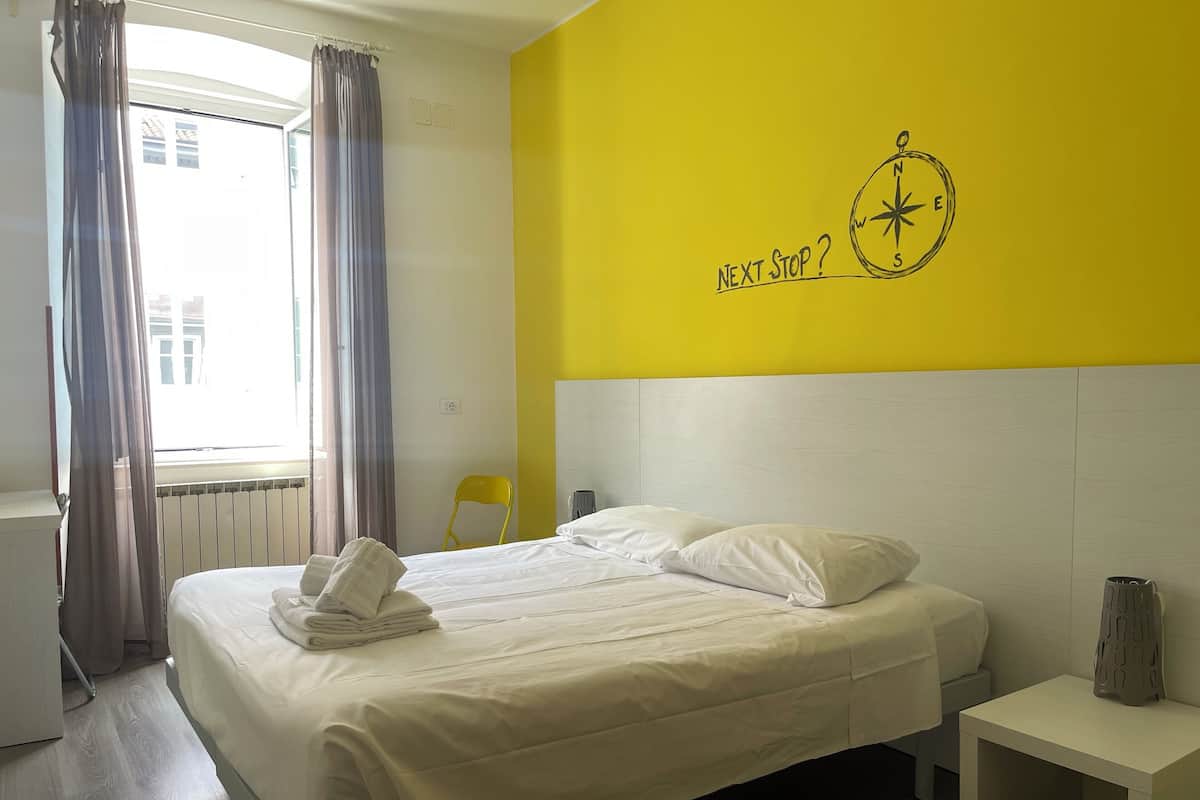 A hotel room with a bed, a nightstand, a chair, and a window with curtains.