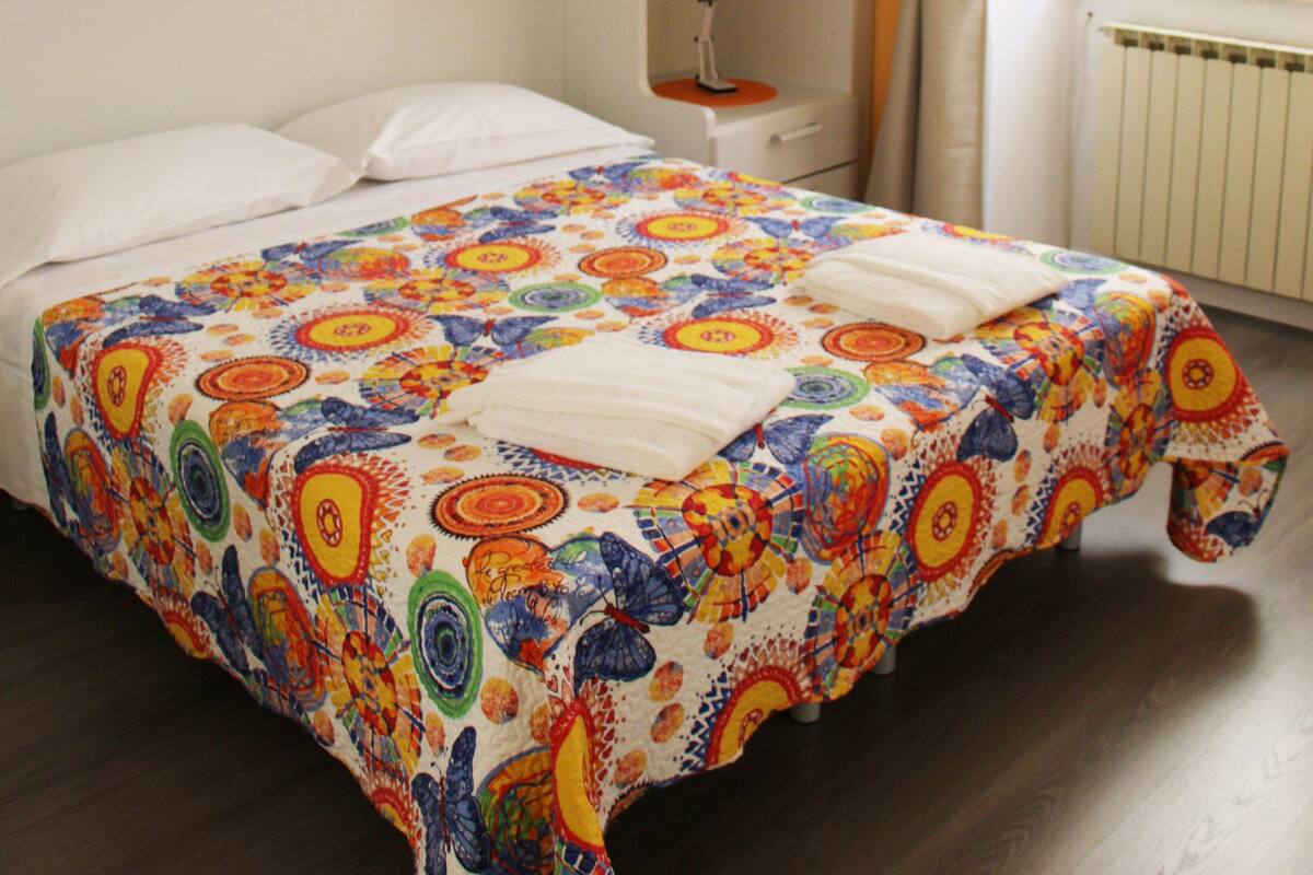 A bedroom with a bed, a bedside table, a lamp, and a window with curtains.