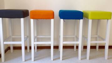 Quatre tabourets de bar blancs, dotés d’assises colorées en noir, orange, bleu et vert.