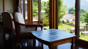 A room with a view of a mountainous landscape through large windows, a wooden table, and two wicker chairs.