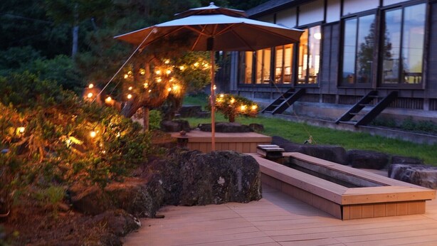 An outdoor deck with a wooden bench, a stone planter, and a pergola with string lights.