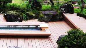 A wooden deck with a rectangular hot tub, surrounded by rocks and greenery.