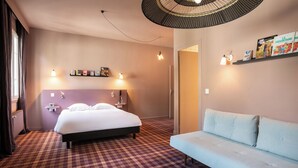 A hotel room with a bed, a sofa, a patterned carpet, wall-mounted lights, and a door leading to another room. - Hôtel Le Beaulieu (Charbonnieres-les-Bains)