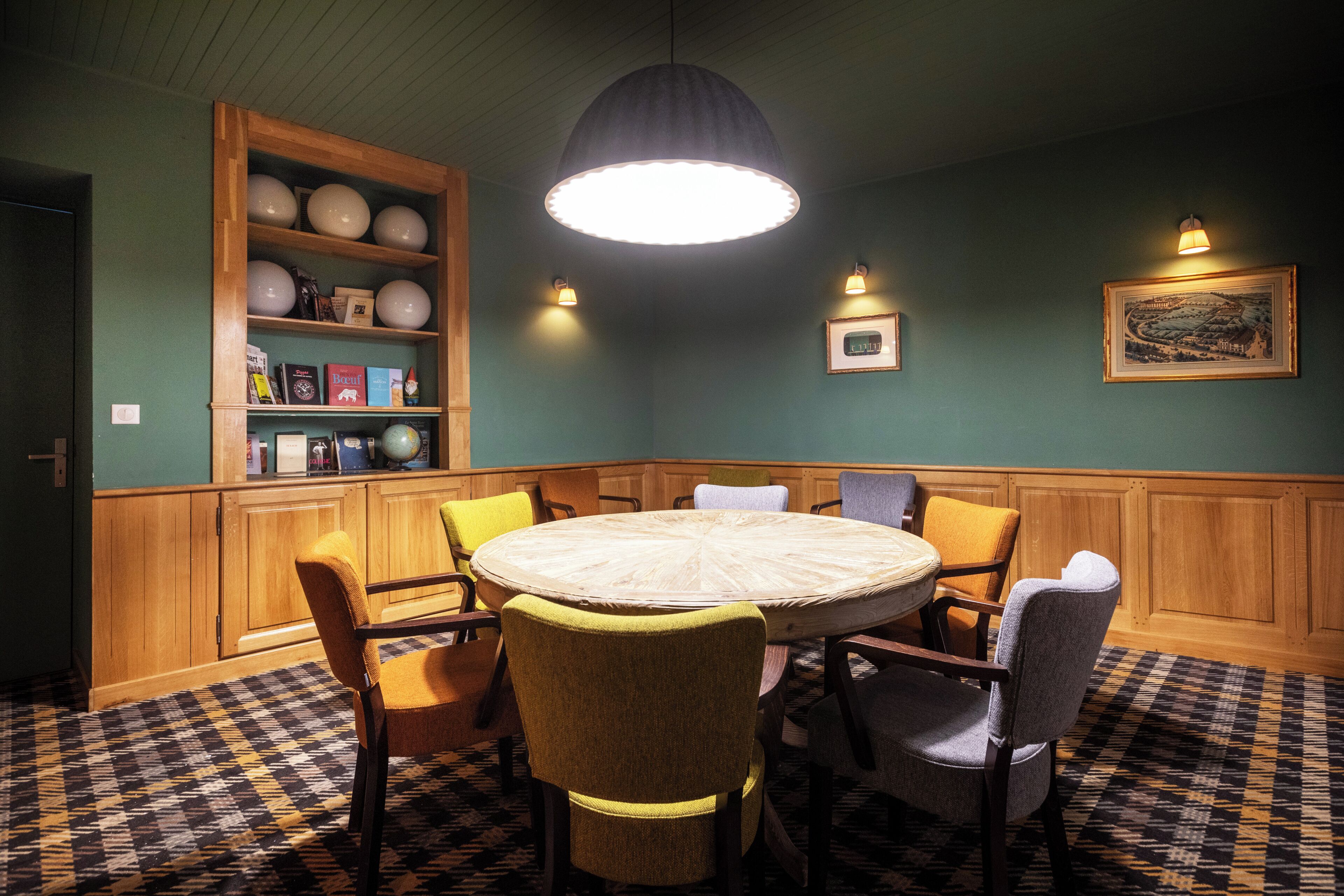 A room with a round table, chairs, a wooden cabinet with shelves, a patterned floor, and wall-mounted lights.