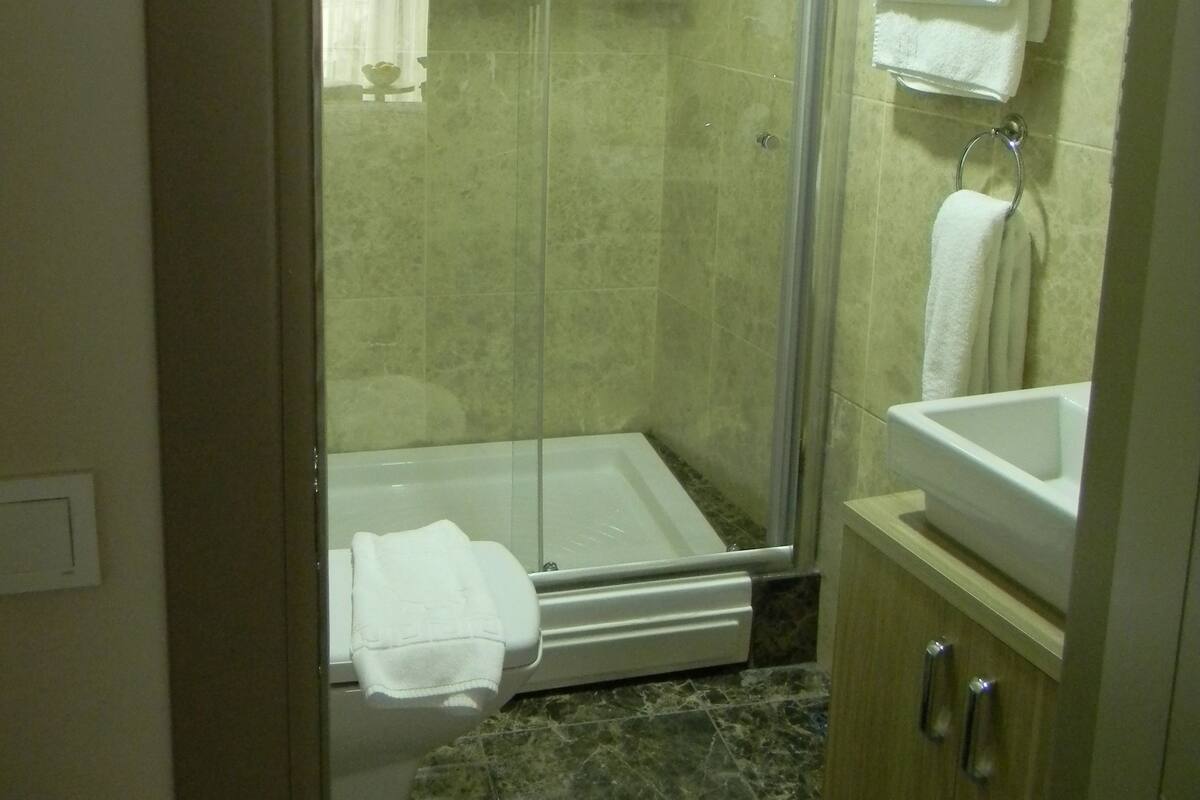 Une salle de bain avec une douche à parois de verre, un lavabo blanc et un sol en marbre.