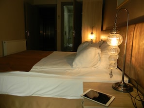 A hotel room with a bed, a bedside lamp, and a tablet on the nightstand.