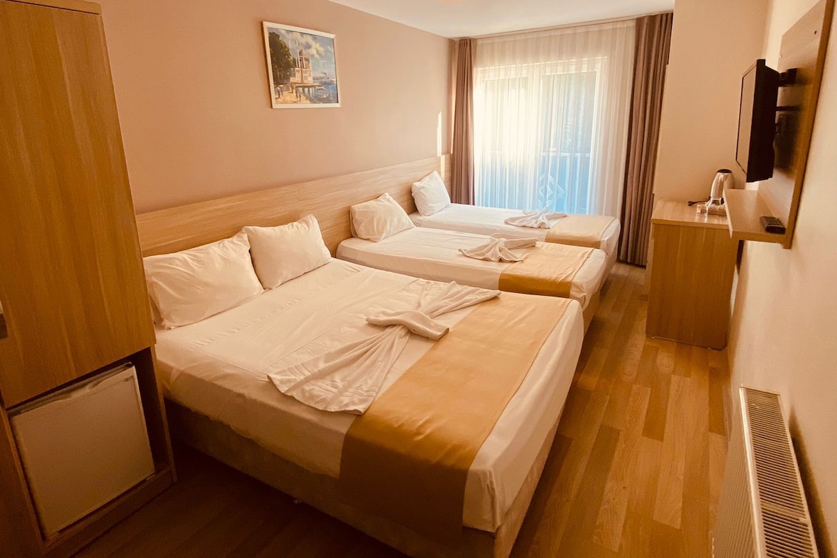 Une chambre d’hôtel avec deux lits, un petit réfrigérateur, un bureau avec un miroir et une fenêtre avec des rideaux.