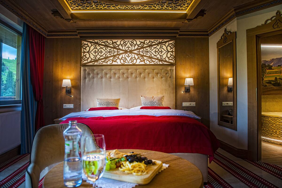 Une chambre d’hôtel avec un grand lit, deux lampes de chevet, une tête de lit en bois et une table à manger où est servi un repas.