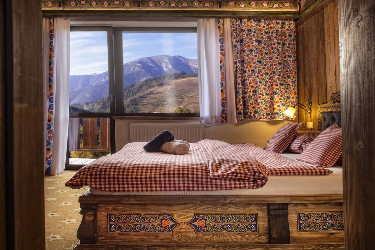 Une chambre à coucher avec un lit, une fenêtre donnant sur les montagnes et des rideaux à motifs.