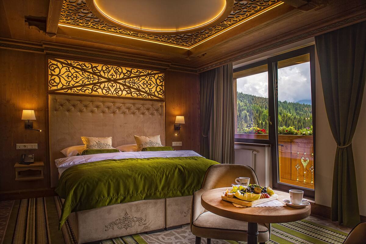 Une chambre d’hôtel avec un grand lit, une petite table où le petit-déjeuner est servi, et une vue sur une forêt par la fenêtre.