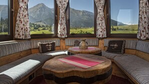 A cozy cabin interior with a large window offering a mountain view, wooden benches, and a central round table with a vase. - Wellness Penzión Strachan (Zdiar)