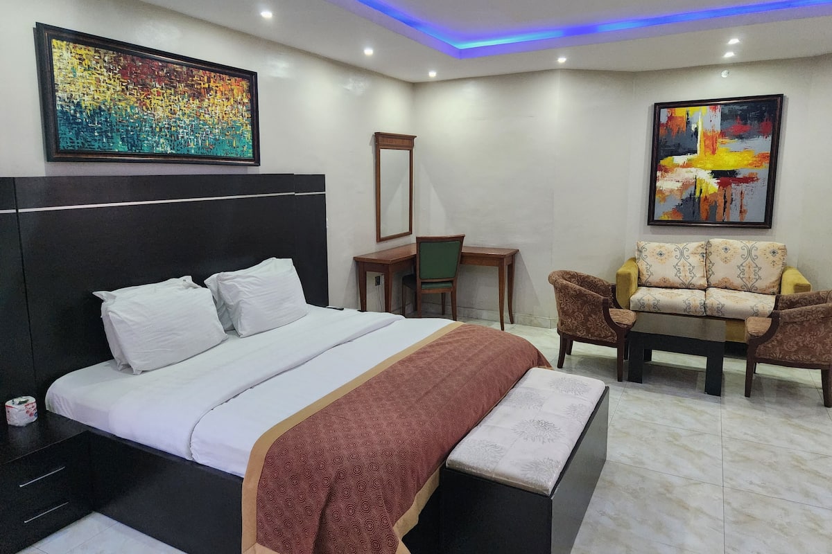 A modern hotel room with a large bed, a desk, and a sofa.