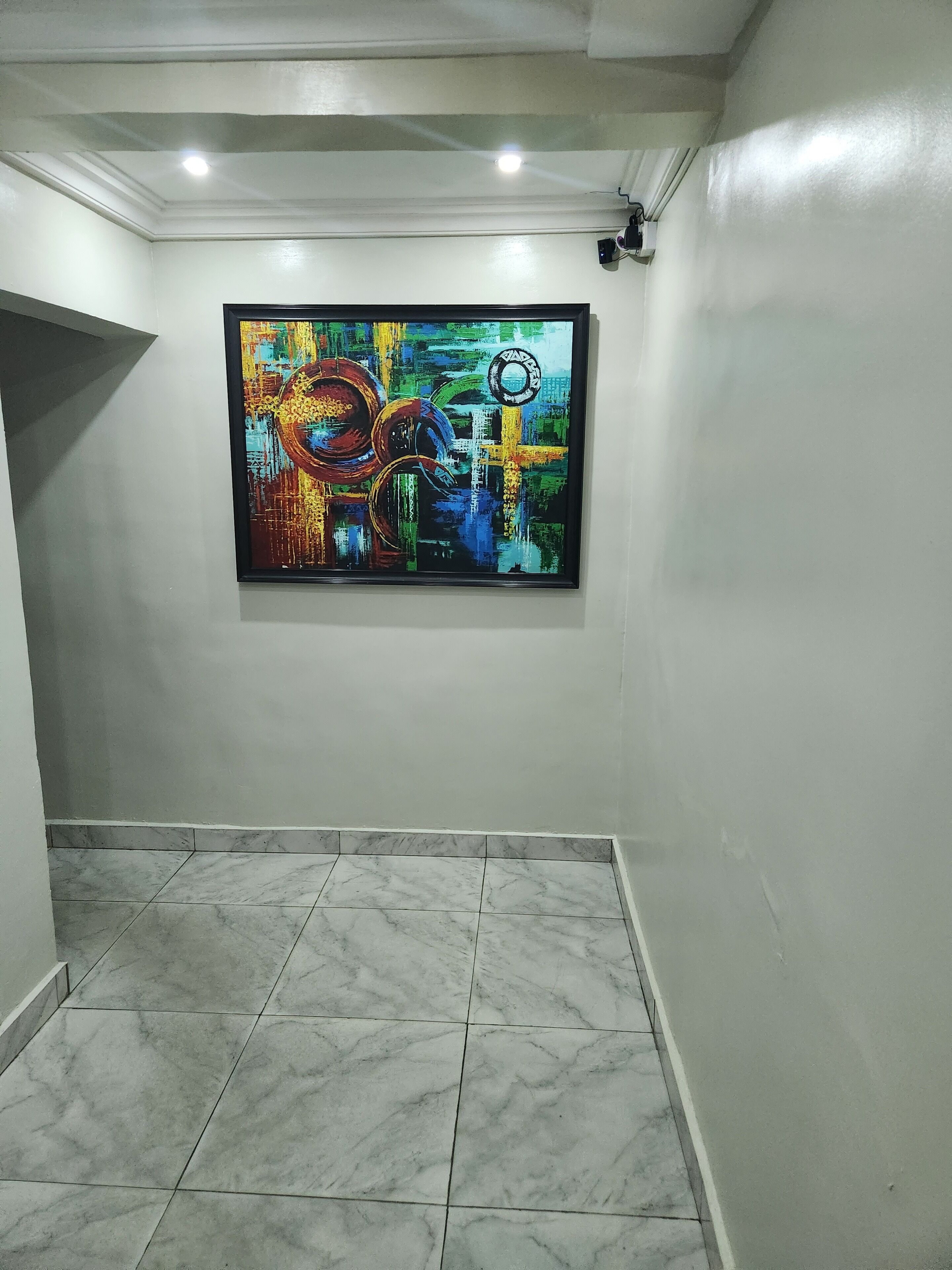 Un couloir doté d’un sol carrelé et orné d’un tableau abstrait encadré au mur.
