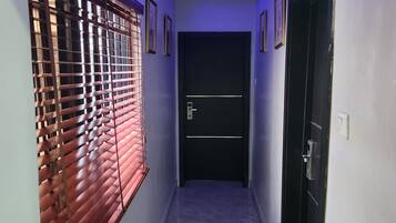 A hallway with a tiled floor, a door with a handle, and a window with blinds.