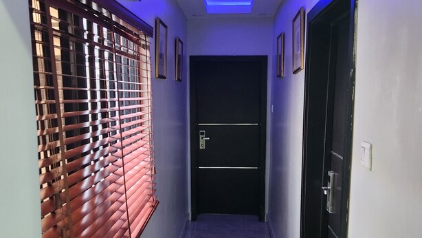 Um corredor com chão de azulejos, uma porta com puxador e uma janela com persianas.
