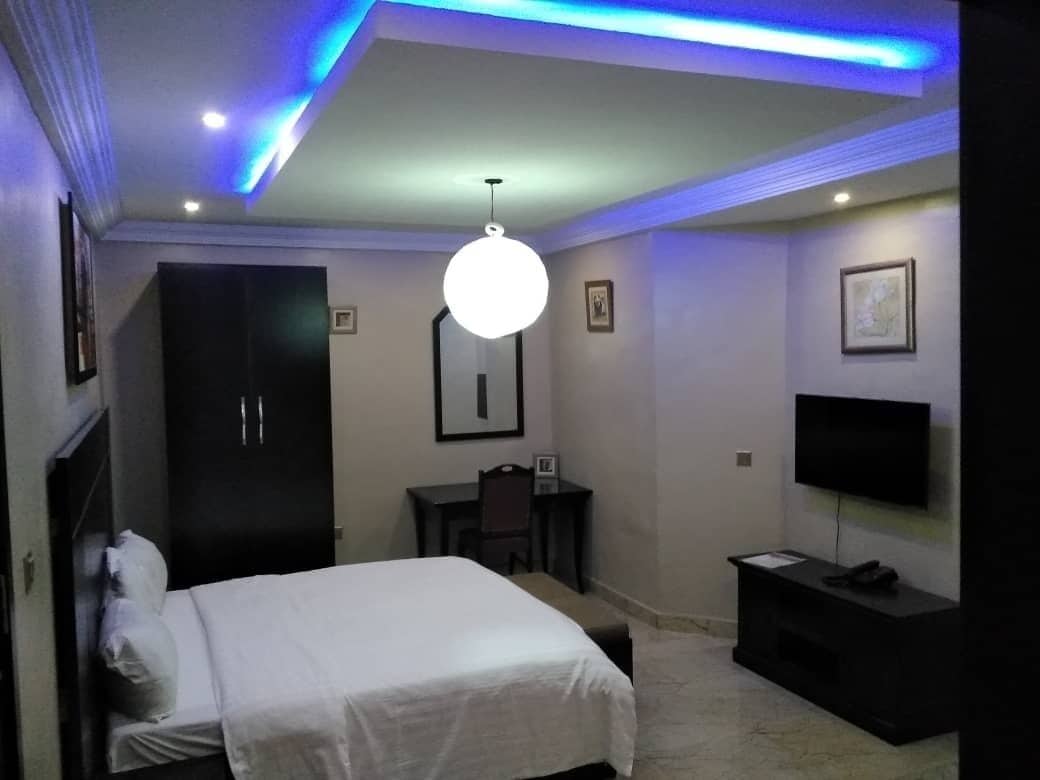 A bedroom with a bed, a desk, a chair, a TV, and a wardrobe.