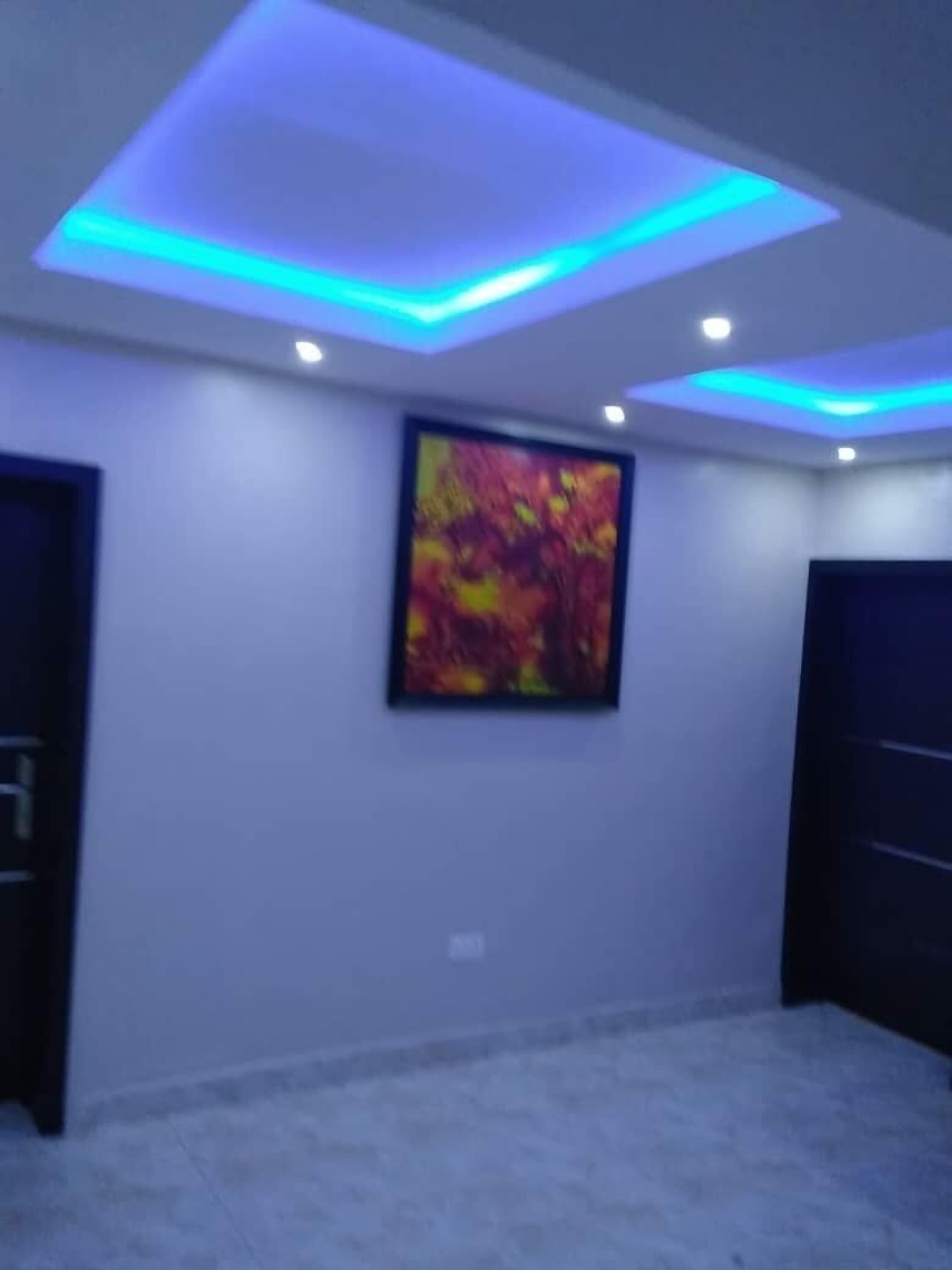 A room with a large abstract painting on the wall, recessed ceiling lighting, and a dark door on the right.
