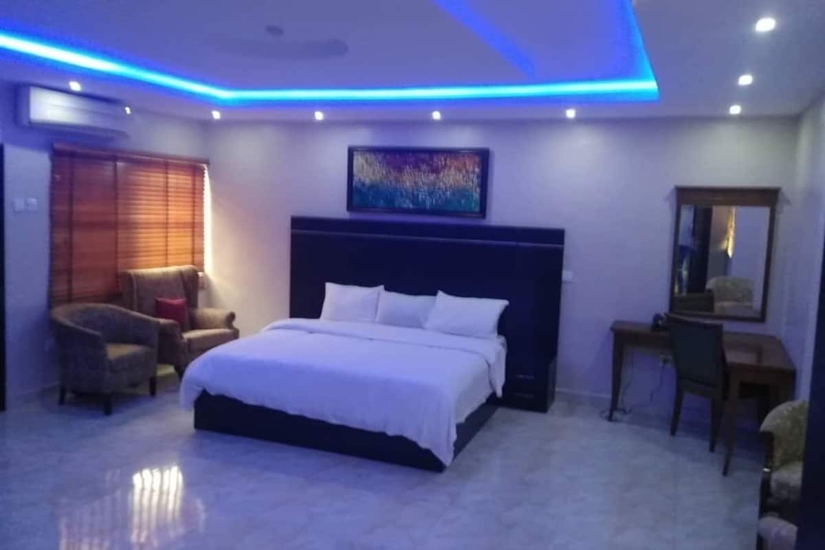A bedroom with a large bed, a desk, a chair, and a painting on the wall.