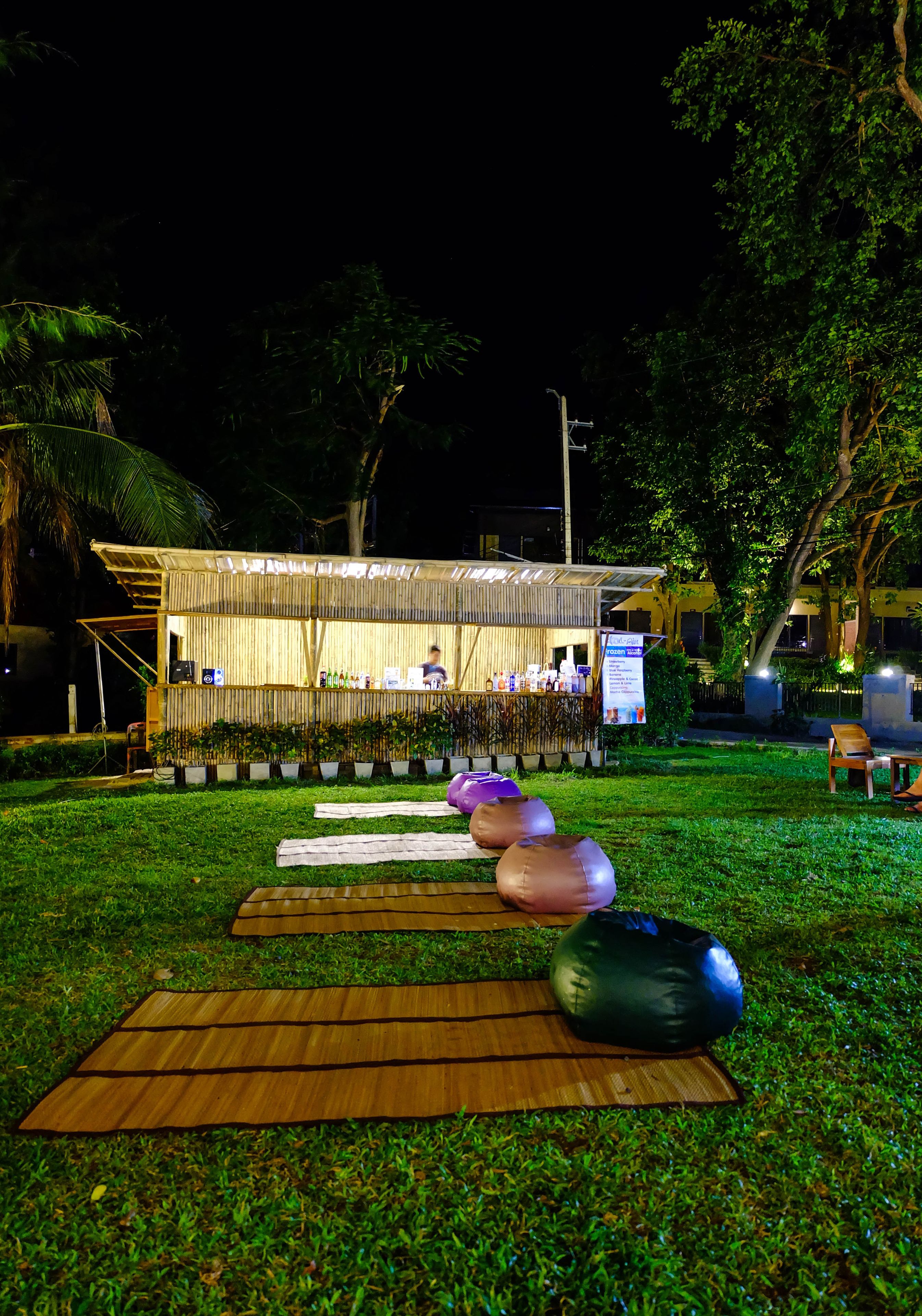 A nighttime outdoor bar area with a bamboo structure, seating, and exercise balls on mats.