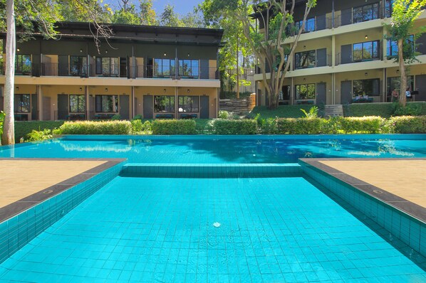 A swimming pool with a tiled edge, surrounded by a landscaped area with bushes and trees.
