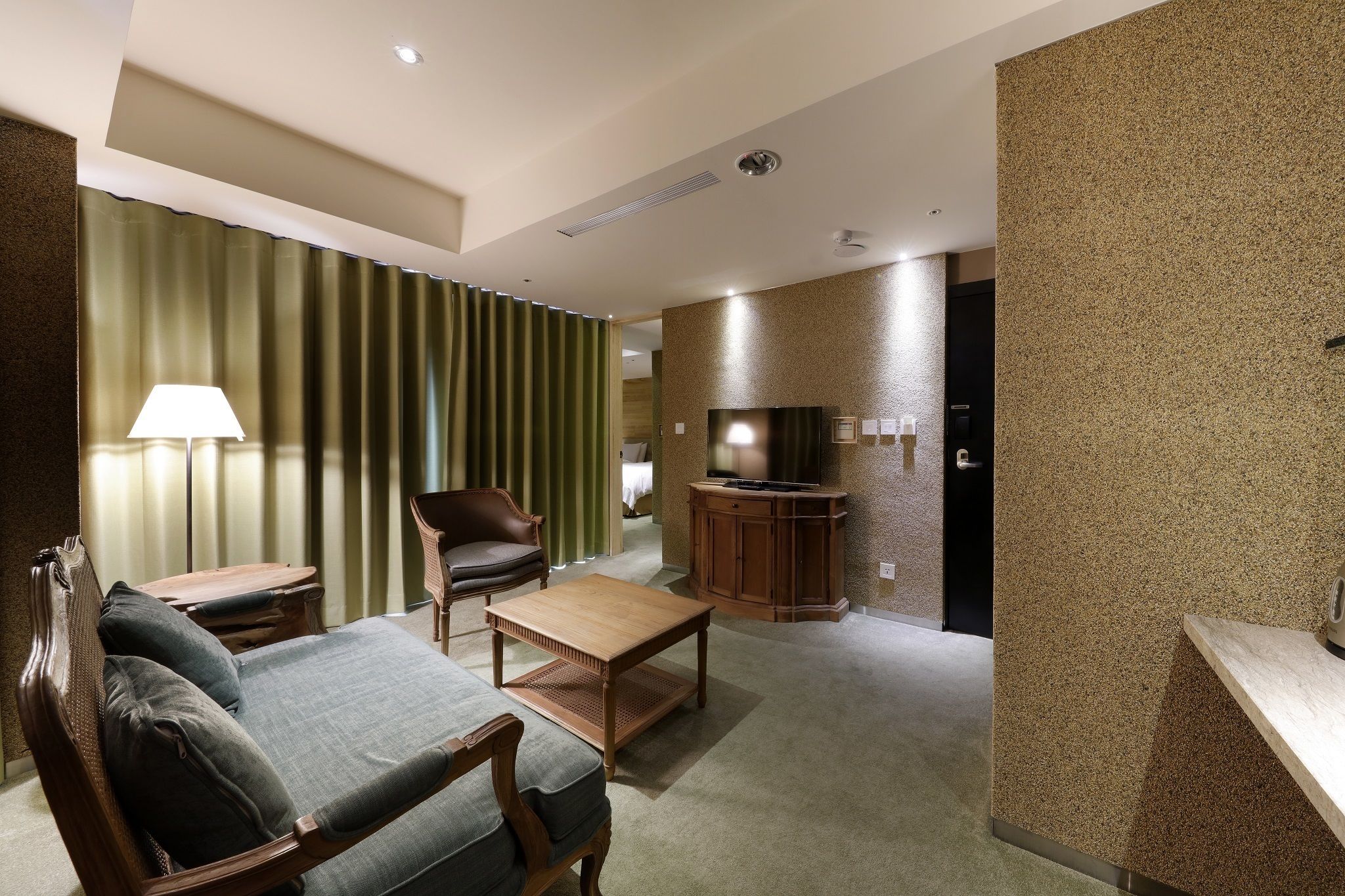 Une chambre d’hôtel équipée d’un canapé, d’un fauteuil, d’une table basse en bois et d’un téléviseur.