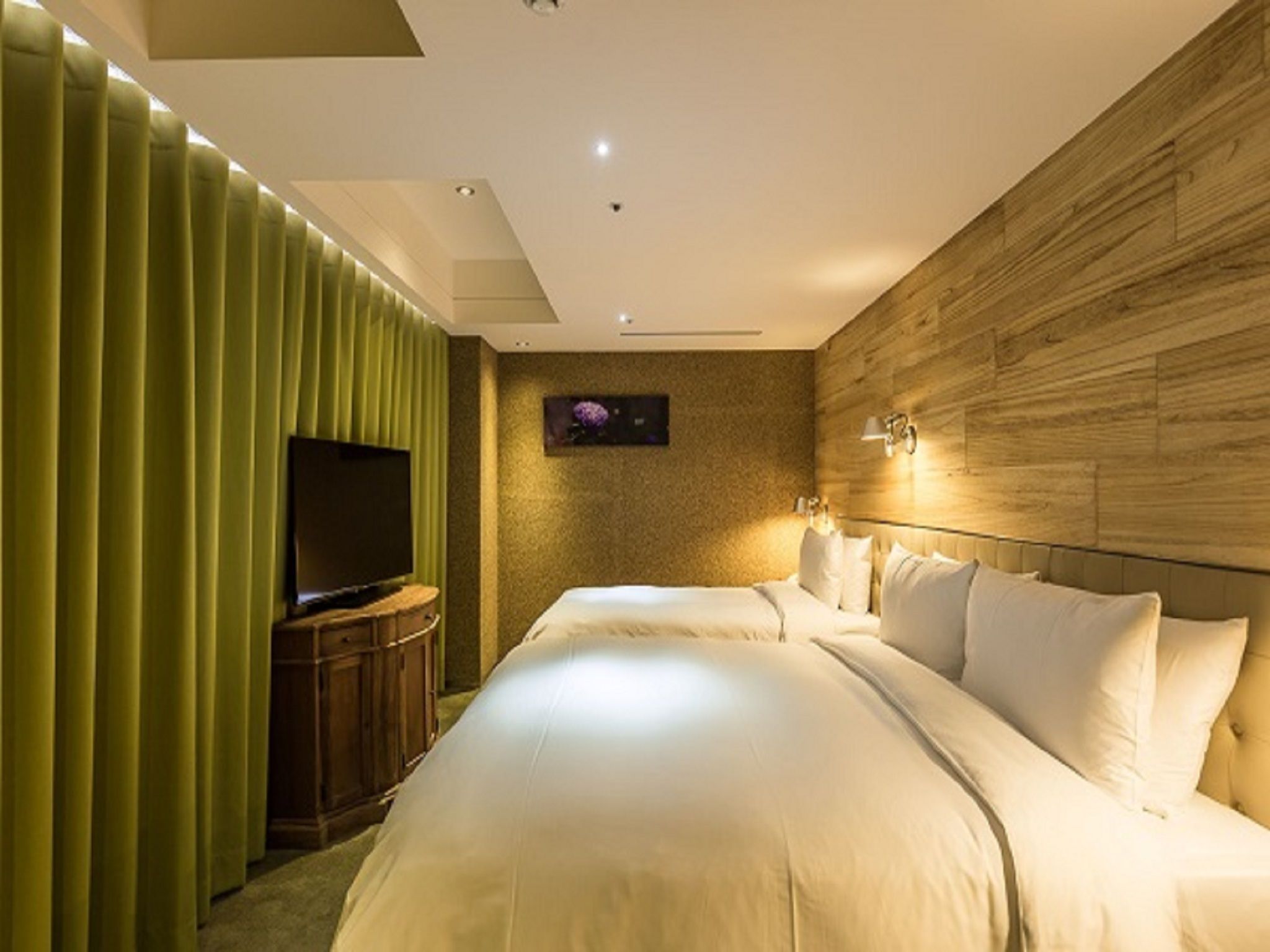 A modern hotel room with a large bed, a television, and a wooden accent wall.