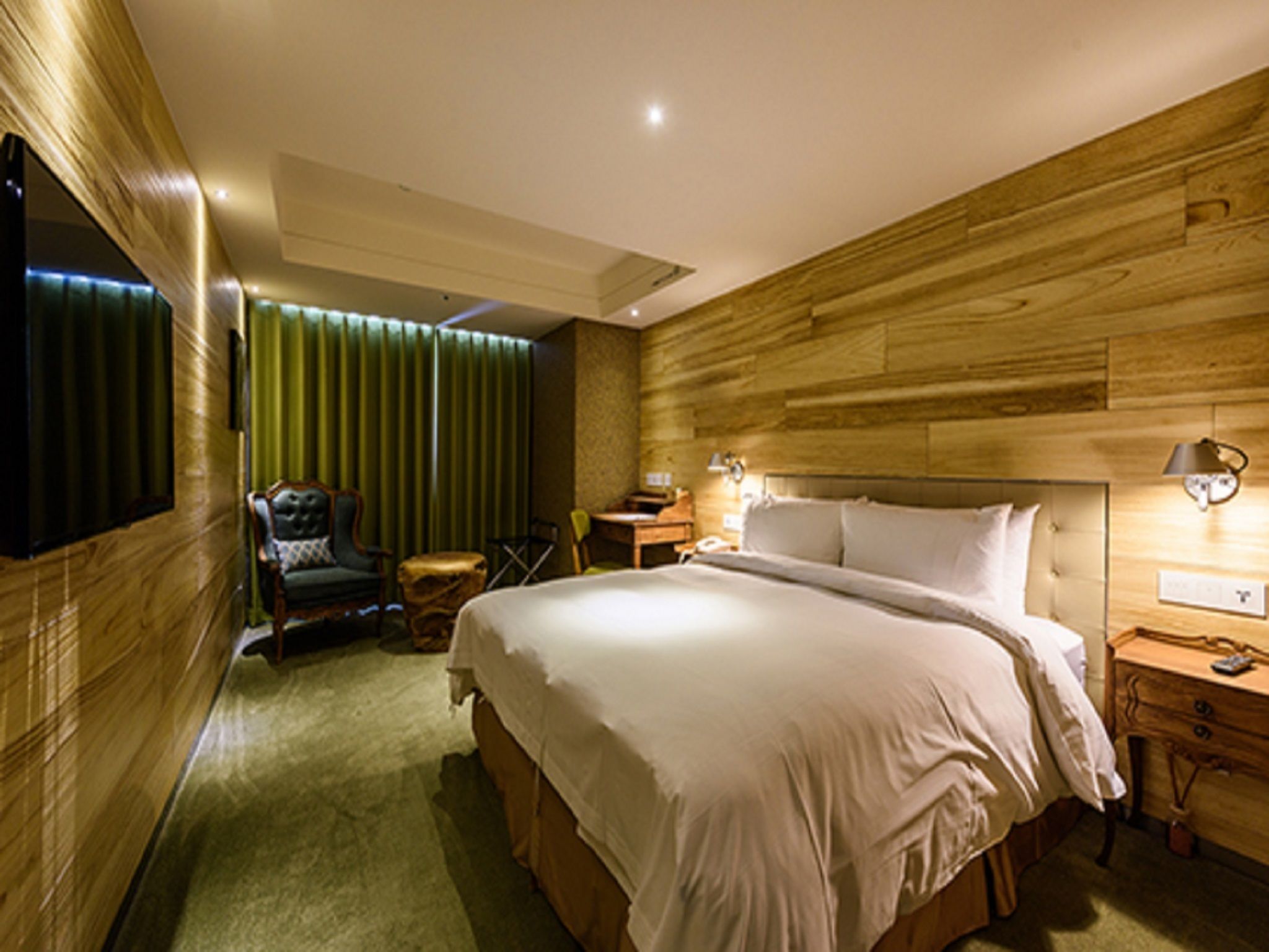 Ein Hotelzimmer mit einem großen Bett, einem Sessel, einem kleinen Tisch und einem an der Wand befestigten Fernseher.