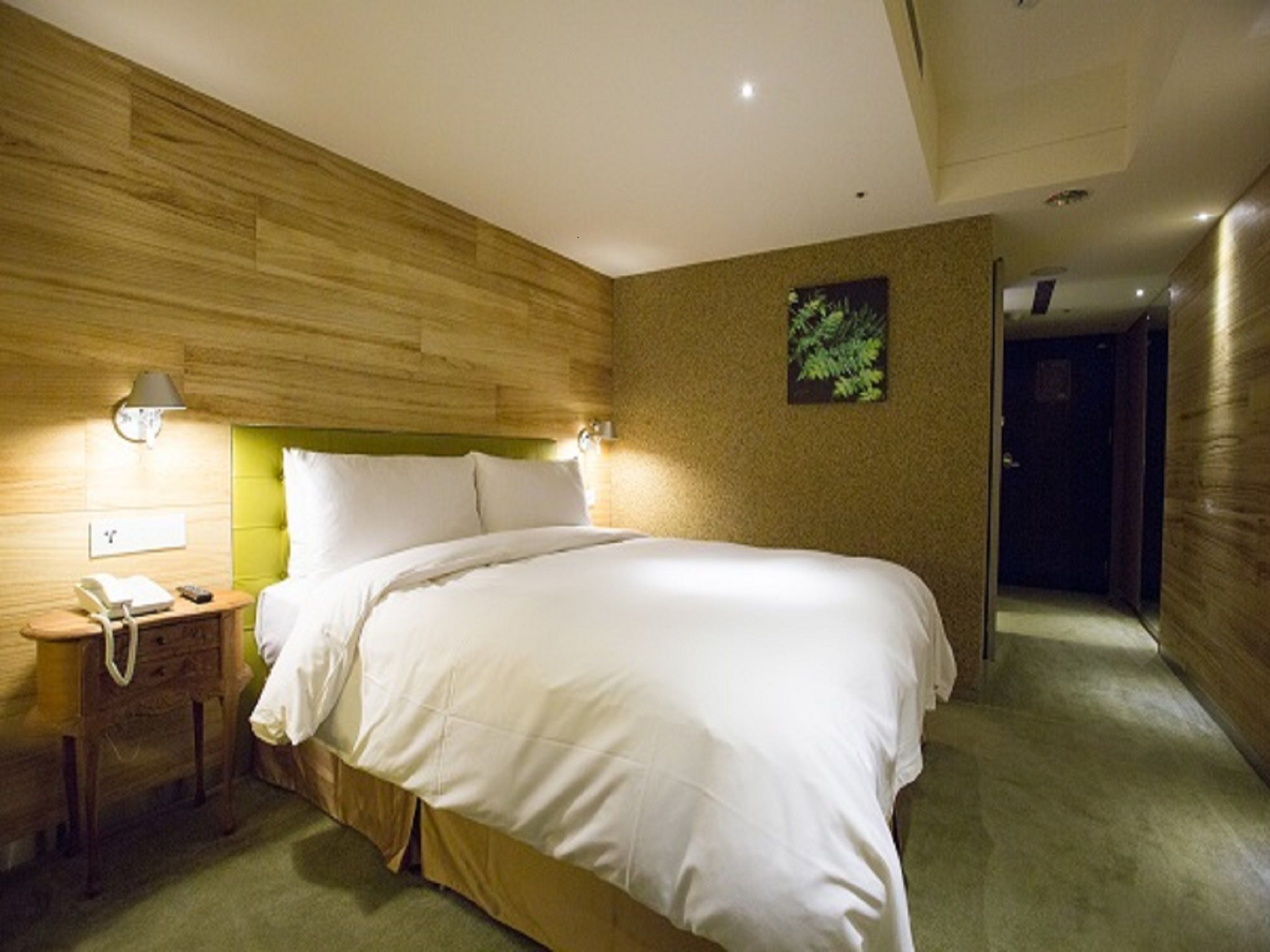 Une chambre d’hôtel avec une tête de lit en bois, une table de chevet avec une lampe, un téléphone et un mur d’accent vert.