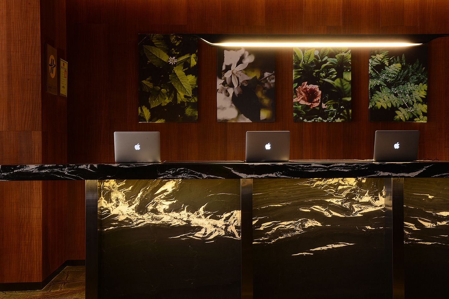 A reception desk with three laptops, wooden panel walls, and framed botanical artwork.