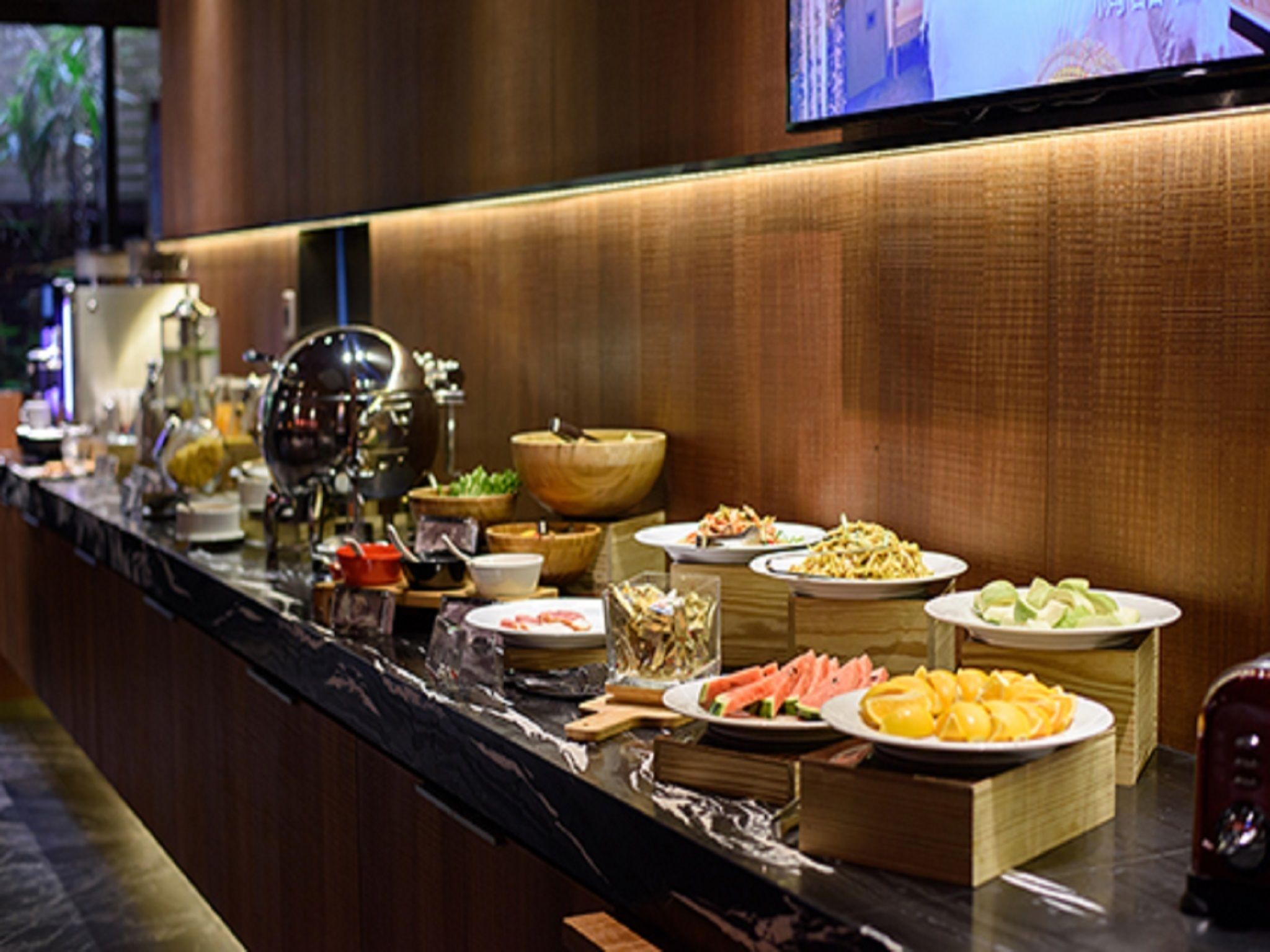 A buffet counter with various dishes and a television screen mounted on the wall.