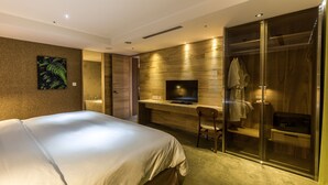 Una habitación de hotel moderna con una cama grande, un escritorio con televisor, zona de ducha y una obra de arte colgada en la pared.