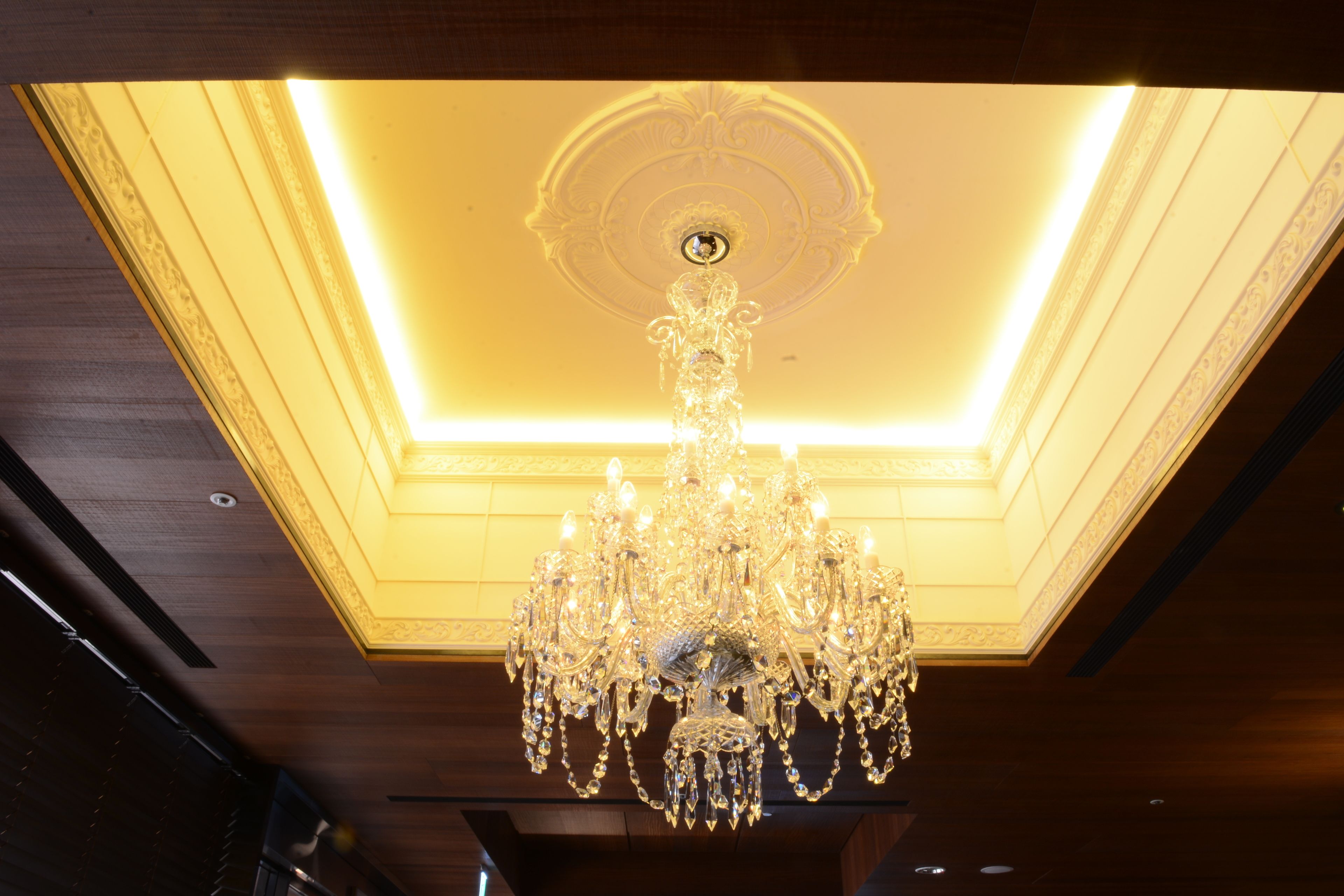 A chandelier with multiple arms and crystal decorations hanging from a ceiling with a recessed light.