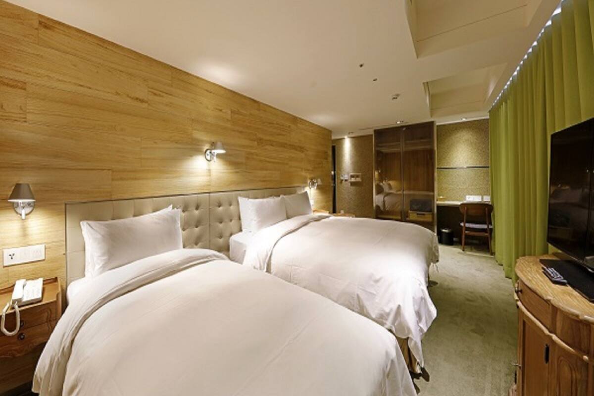 A hotel room with two beds, a wooden headboard, a TV, and a green curtain.