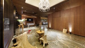 Un vestíbulo amplio con candelabro, suelo de madera y una zona de estar con planta y una mesita.