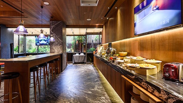 Zona de bar con taburetes de madera, suelo de mármol y una barra con alimentos.