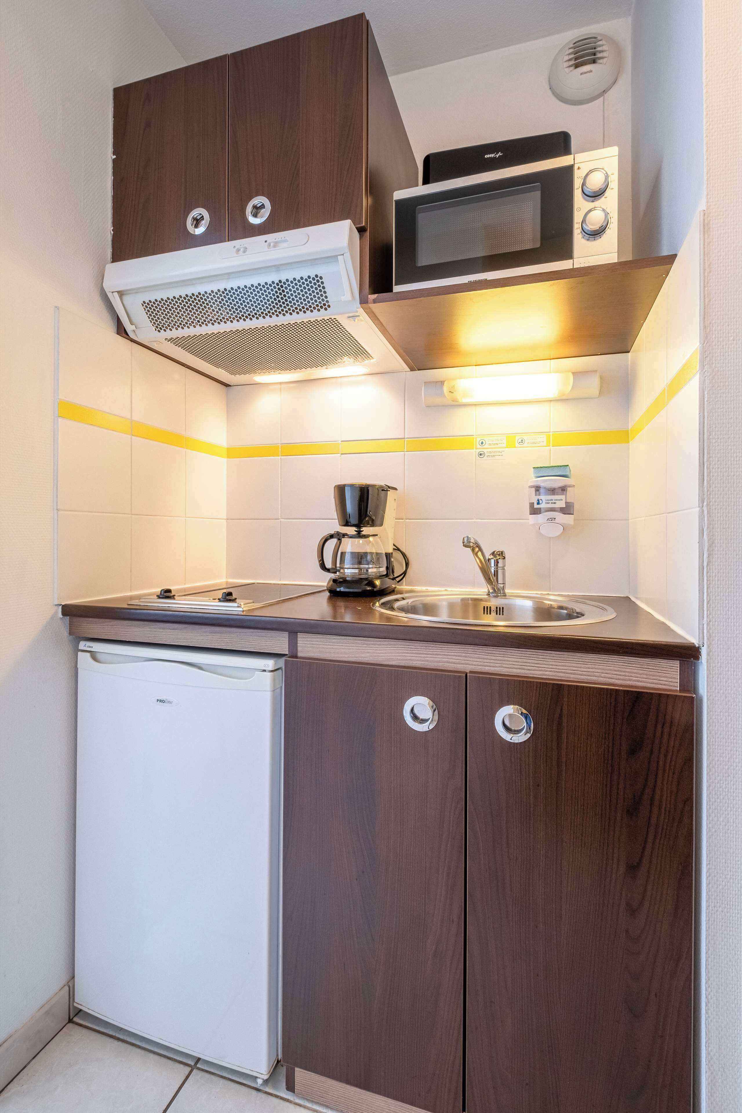 Una kitchenette compacta con microondas, cafetera y un refrigerador pequeño.