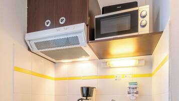 Una kitchenette compacta con microondas, cafetera y un refrigerador pequeño.