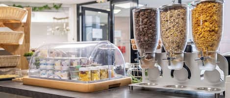 Un buffet où les clients peuvent se servir eux-mêmes pour le petit-déjeuner, avec un choix varié d’aliments et une machine à café.