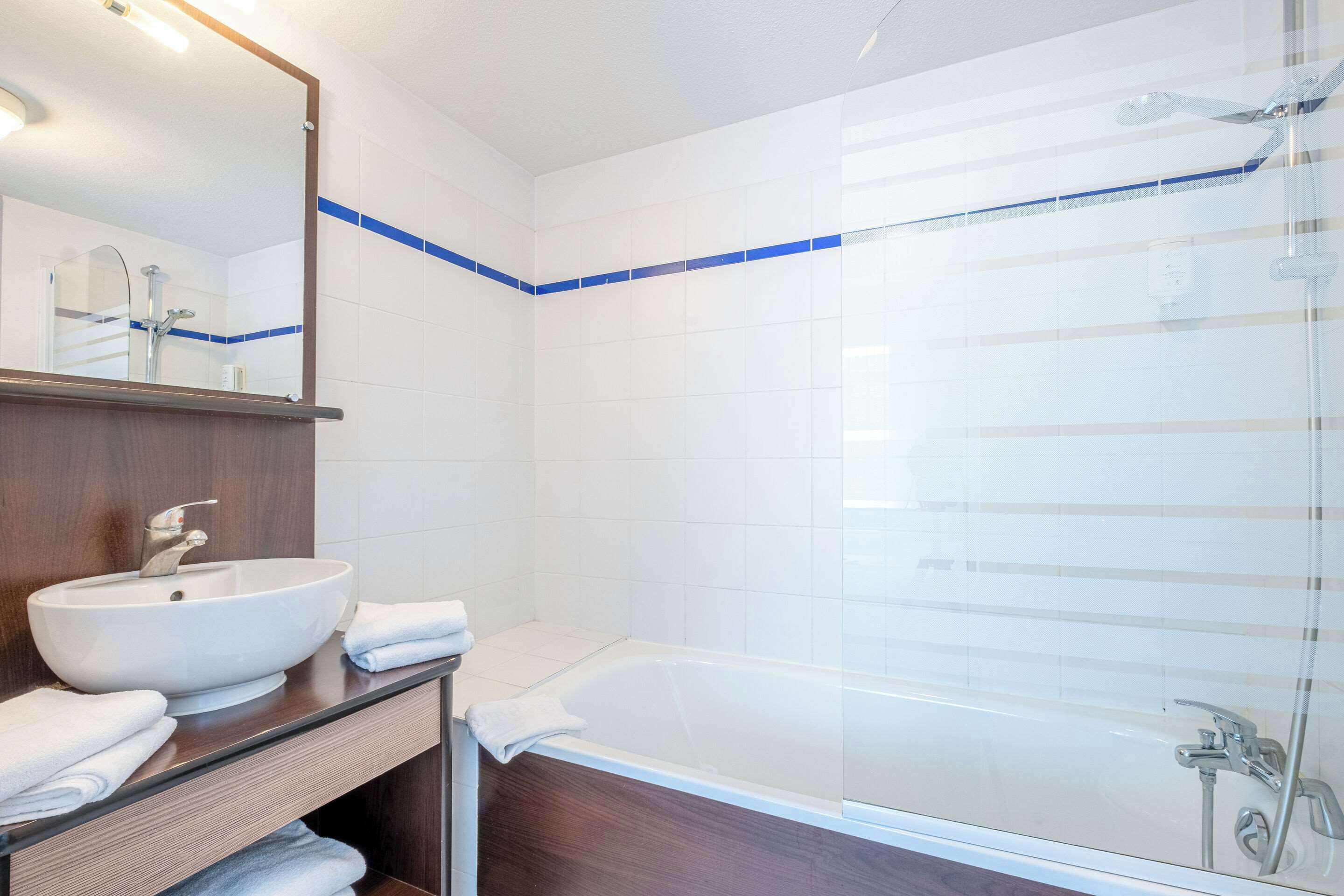 Une salle de bain moderne avec un lavabo blanc, un miroir, une baignoire et une douche.