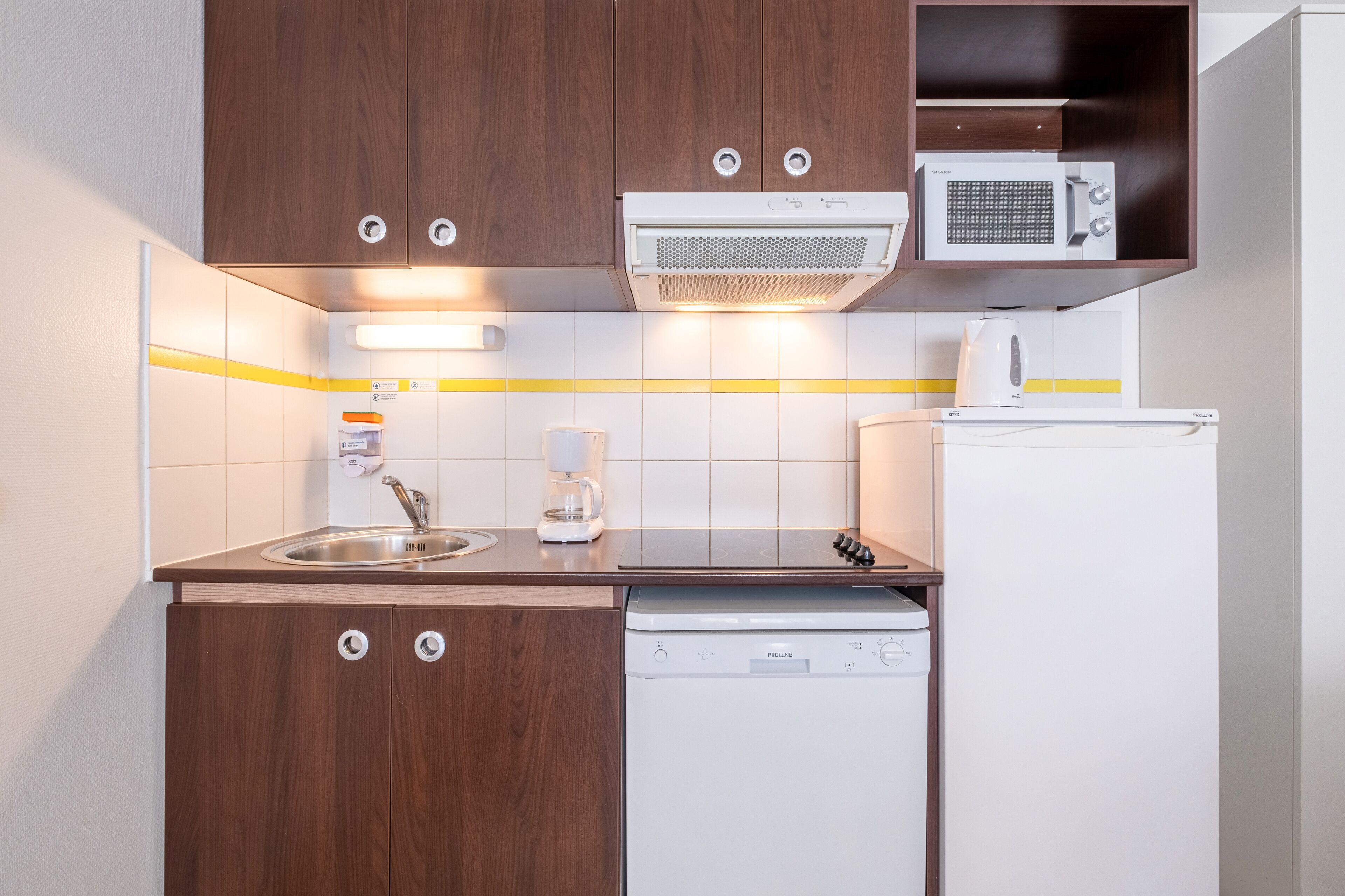 Una cocina compacta con armarios de madera, microondas, cafetera y lavavajillas.